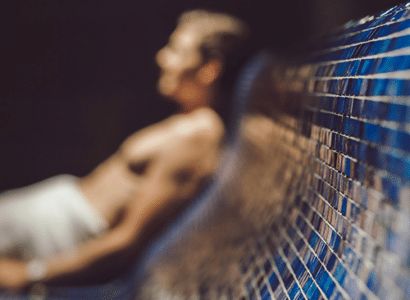 Eine Person lehnt sich an eine blaue Mosaikwand in der Therme Wien, entspannt und das Ambiente der Sauna geniessend.
