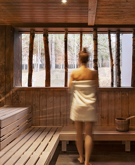 Frau in der Sauna mit Handtuch umwickelt schaut aus dem Fenster