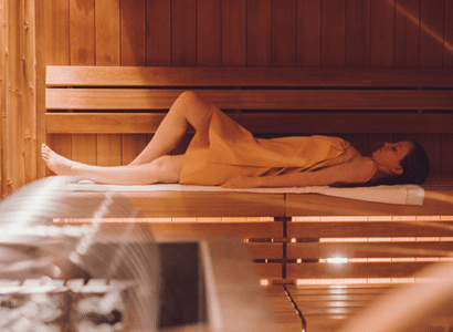 Eine junge Frau liegt in einer Sauna der Therme Wien, entspannt und in ein Handtuch gehuellt, waehrend die warme Beleuchtung für eine behagliche und friedliche Atmosphaere sorgt.