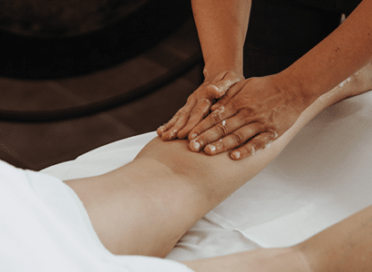 Eine Person fuehrt gerade eine Lymphdrainage durch an einer Frau, die auf der Massagebank liegt.