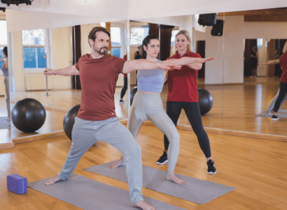Zwei Personen nehmen an einem Yoga- oder Fitnesskurs in der Therme Wien Fitness teil, ausgeführt in koordinierten Posen auf Yogamatten und betreut von einer Trainerin.