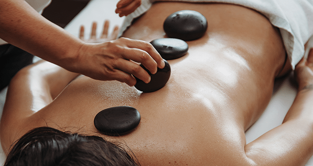 Hot stones werden waerend einer Massage auf den Ruecken einer Frau gelegt.