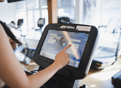 Eine Person interagiert mit einem digitalen Trainingsgeraet im Fitnesscenter der Therme Wien. Auf dem Bildschirm sind verschiedene Trainingsprogramme zu sehen, die eine individuelle und interaktive Trainingserfahrung ermöglichen.