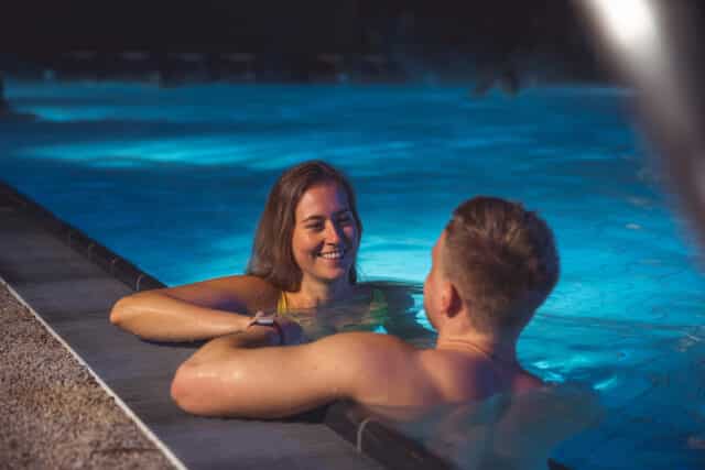 Junges paar liegt entspannt an einem Sommerabend outdoor in einem Becken der Therme Wien.