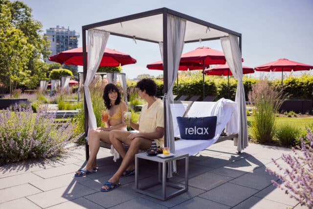 Junge Frau und junger Mann sitzen in einem Himmelbett der Relax! Lounge im Garten der Inspiration und trinken Cocktails.