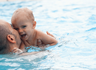 Kleinkind und Vater im Wasser beim Schwimmkurs für BABY üben Schwimmen