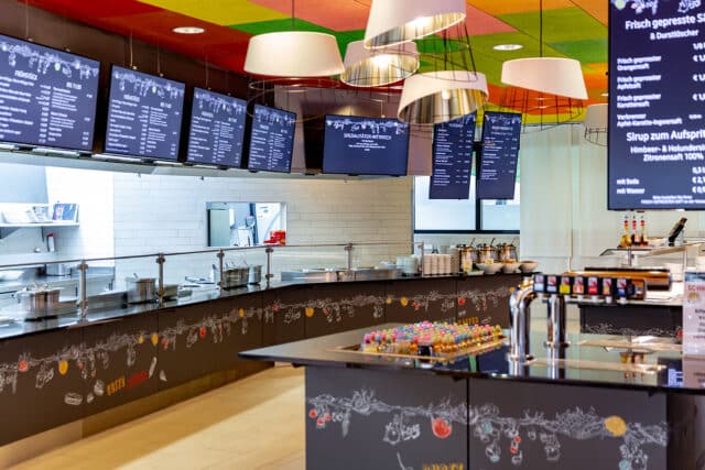 Thermewien restaurant mit BIldschirmen auf denen Speisen in weisser Schrift auf schwarzem Hintergrund zur Auswahl angezeigt werden.